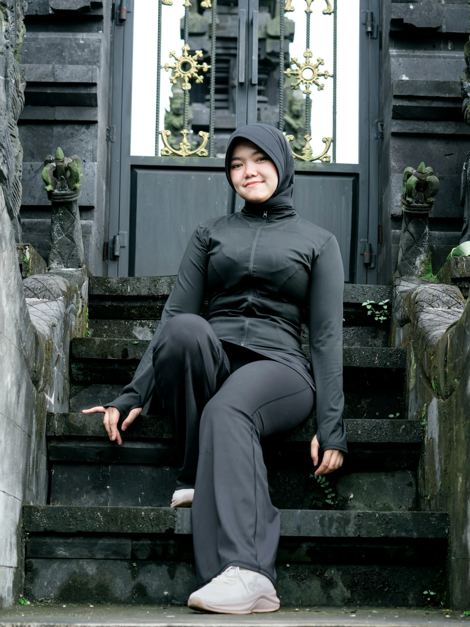 Woman in modest long-sleeve activewear and flared leggings, seated on stone steps